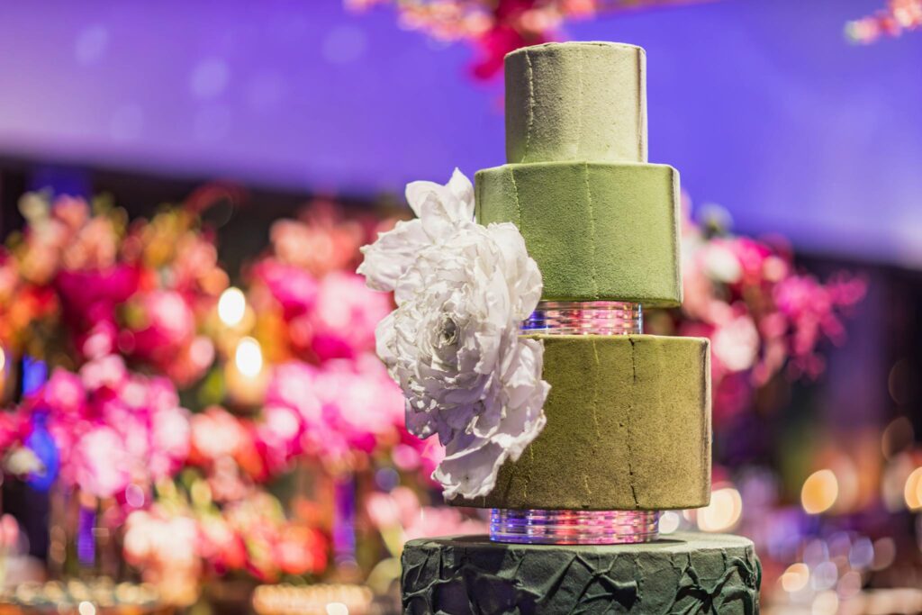 Luxurious green three-tier cake with large white floral decoration, perfect for elegant celebrations.